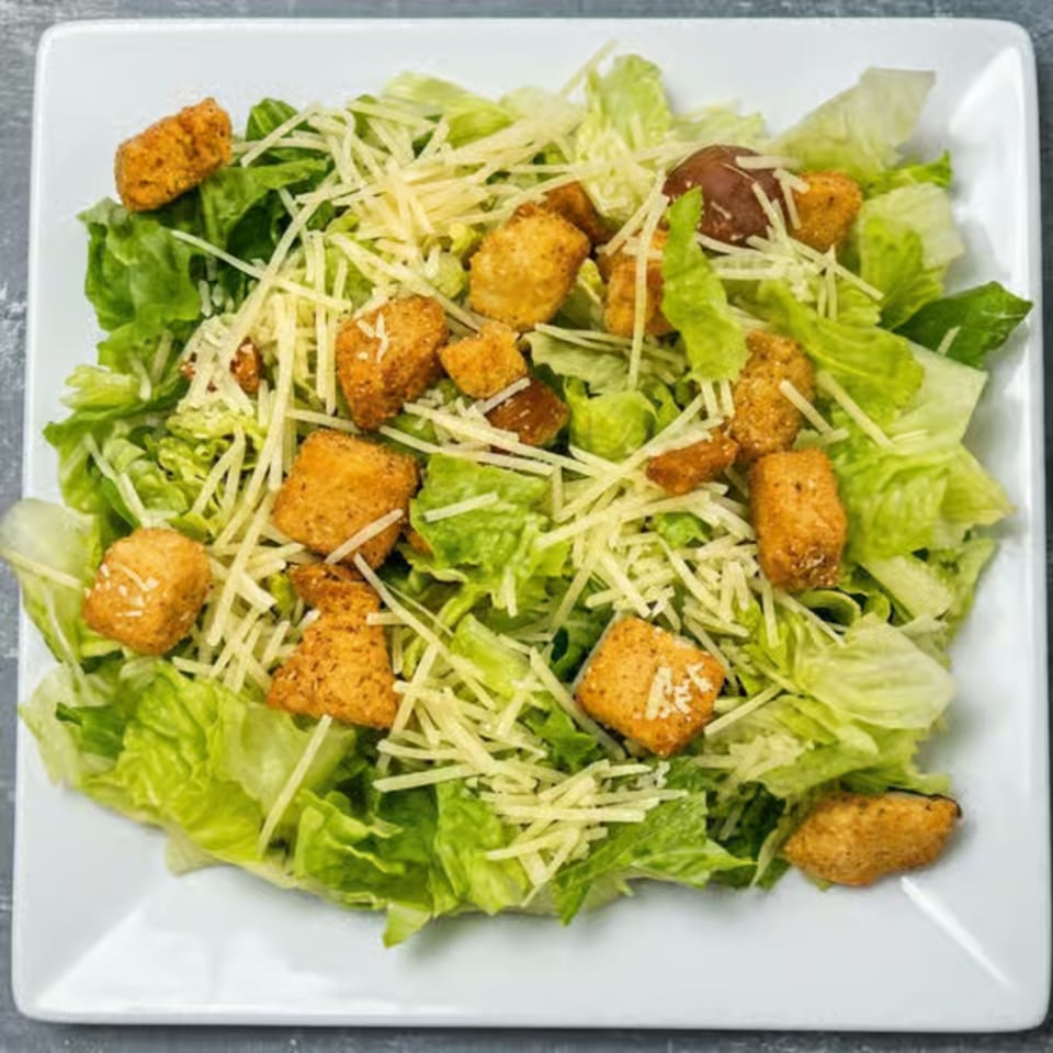 Caesar salad with crisp romaine lettuce, crunchy croutons, and shredded Parmesan cheese on a white plate.