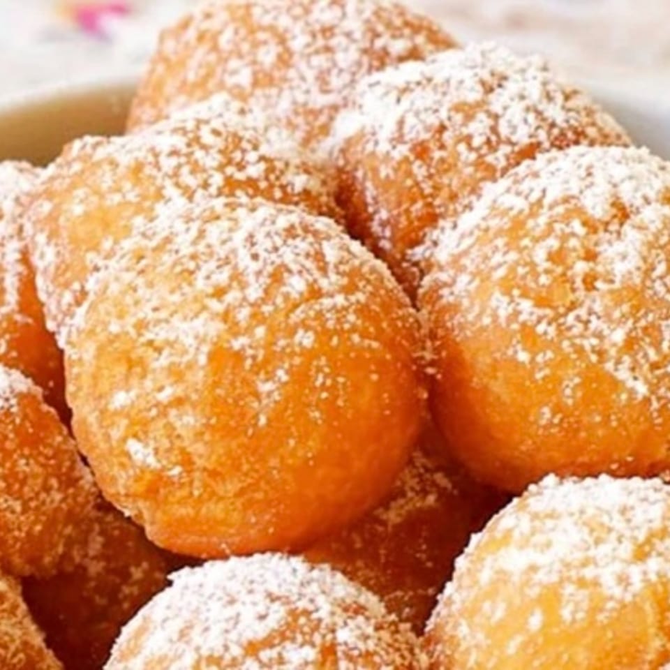 Close-up of golden-brown fried dough balls, generously dusted with powdered sugar.