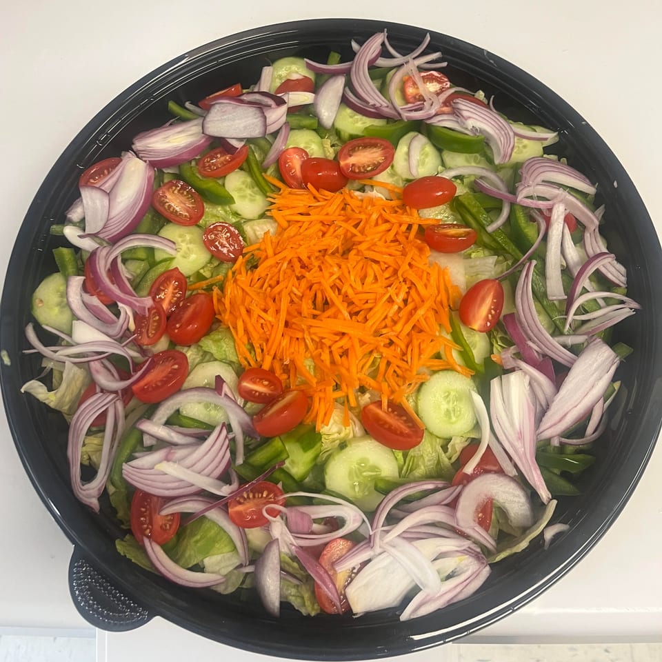 A large black bowl filled with a fresh garden salad, topped with shredded carrots, tomatoes, and red onions.